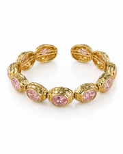 A gold cuff bracelet featuring oval pink gemstones in textured bezel settings, displayed on a clean white background.