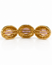 A gold three-piece cuff bracelet featuring three textured oval links with light pink gemstone inlays, shown on a reflective white background.