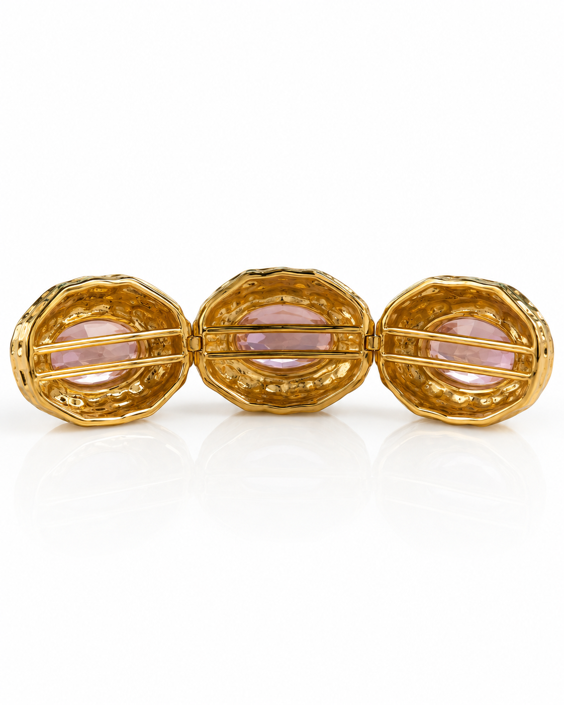 A gold three-piece cuff bracelet featuring three textured oval links with light pink gemstone inlays, shown on a reflective white background.